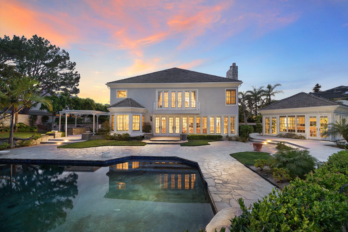 Twilight real estate photo of a two-story home with a lit pool at dusk